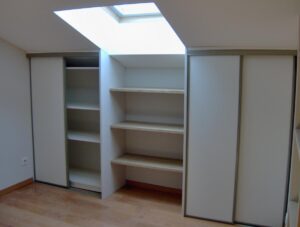 Aménagement de rangement sous une lucarne de toit, avec étagères ouvertes au centre et placards à portes coulissantes blanches sur les côtés.