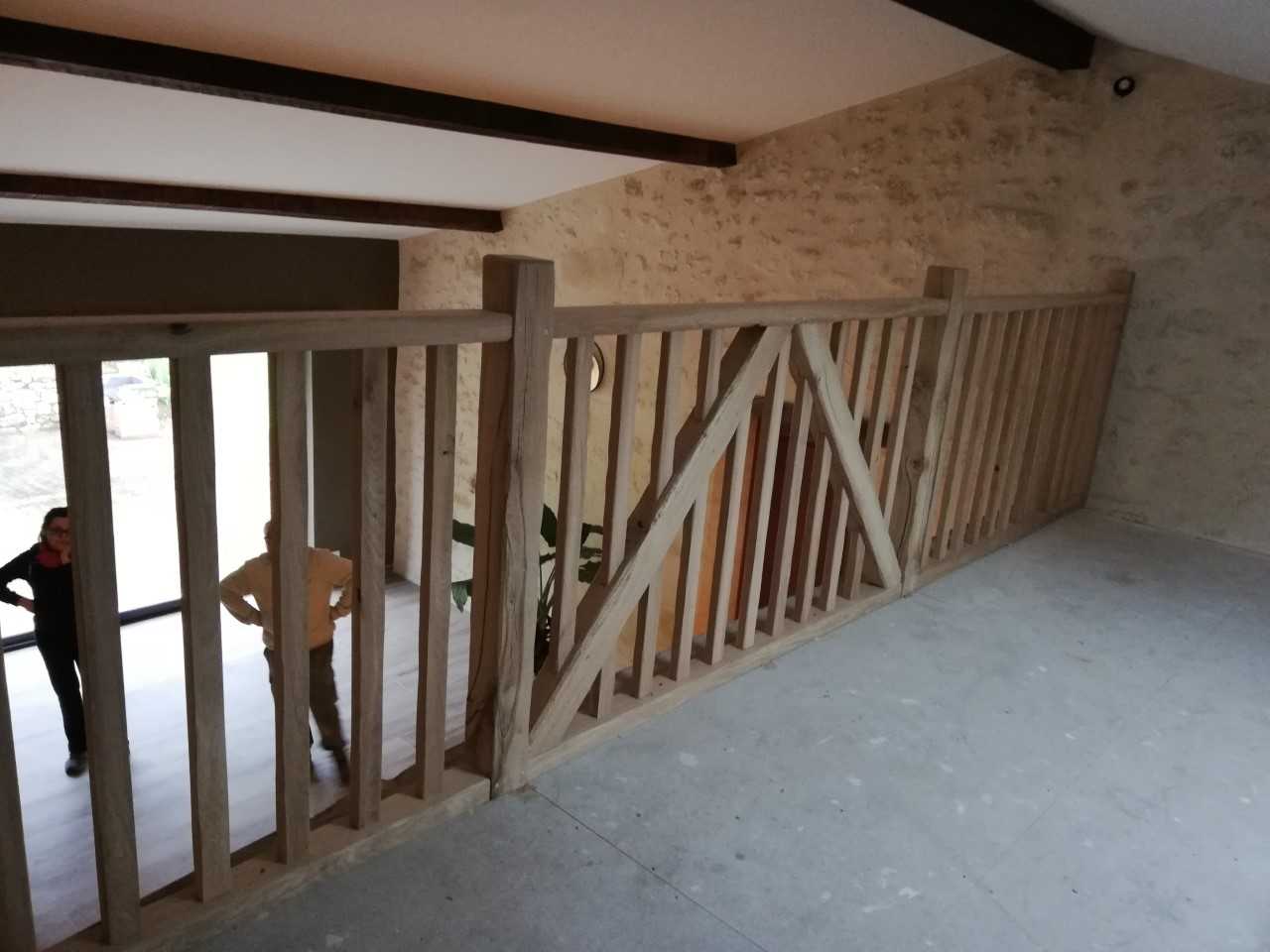 Garde-corps en bois massif sur une mezzanine avec design en croix, surplombant un intérieur moderne en pierre.