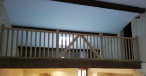 Garde-corps en bois sur mesure pour mezzanine avec portillon de sécurité et poutres apparentes rustiques.