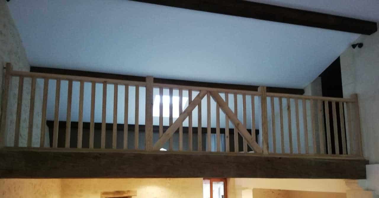 Garde-corps en bois sur mesure pour mezzanine avec portillon de sécurité et poutres apparentes rustiques.